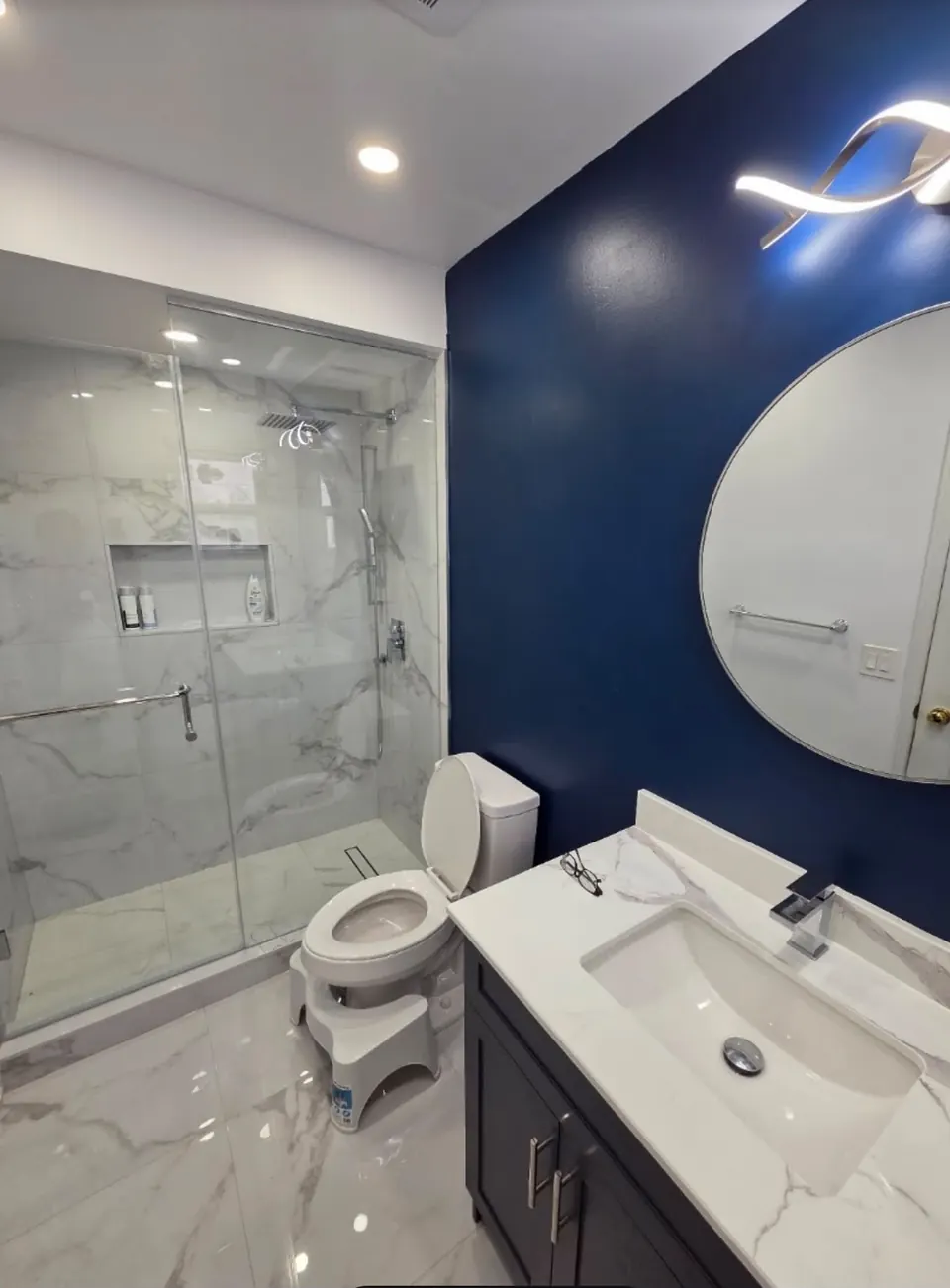 Bathroom with navy feature wall, round mirror and glass shower