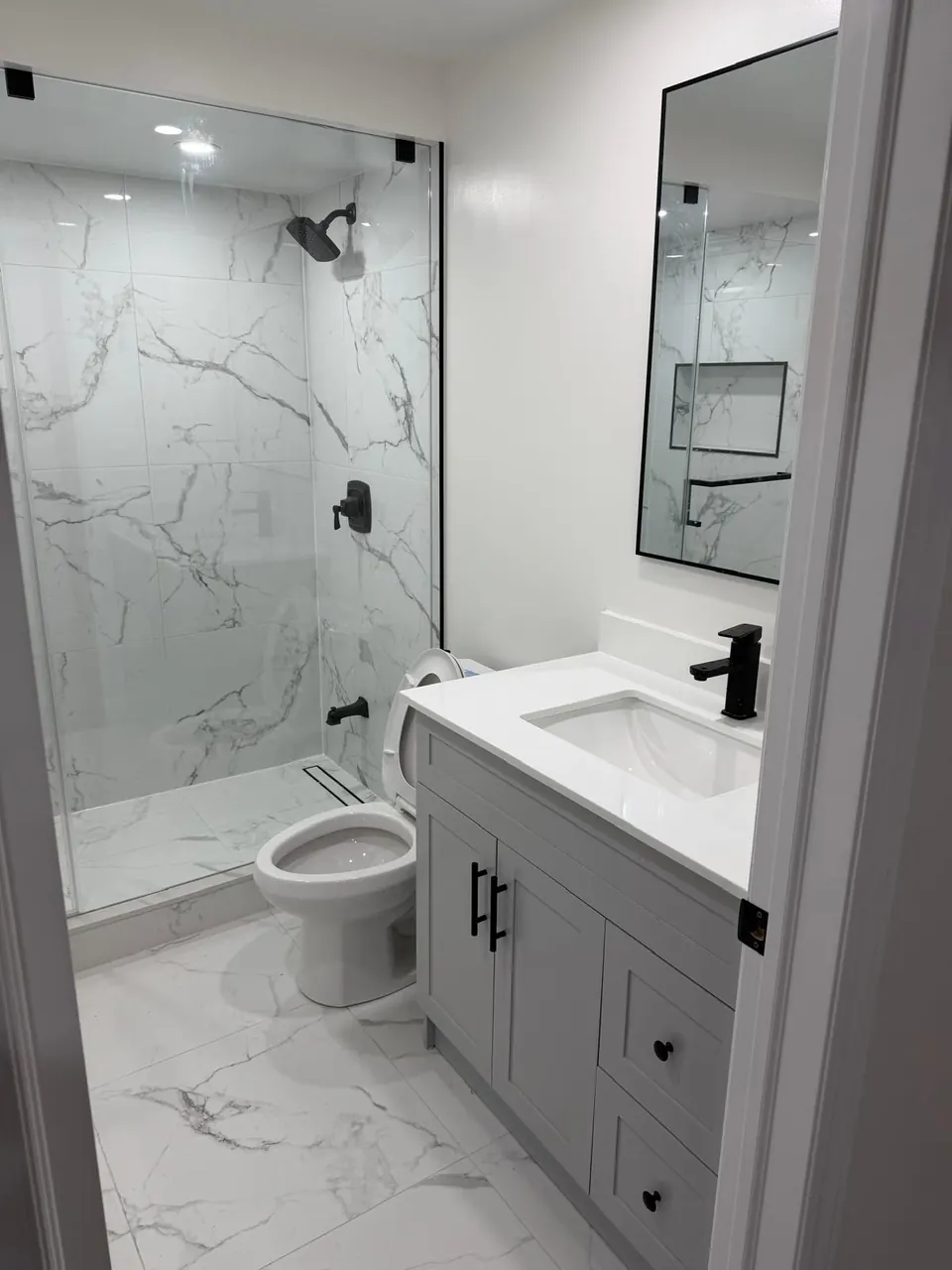 Compact bathroom with glass shower, toilet and shaker vanity