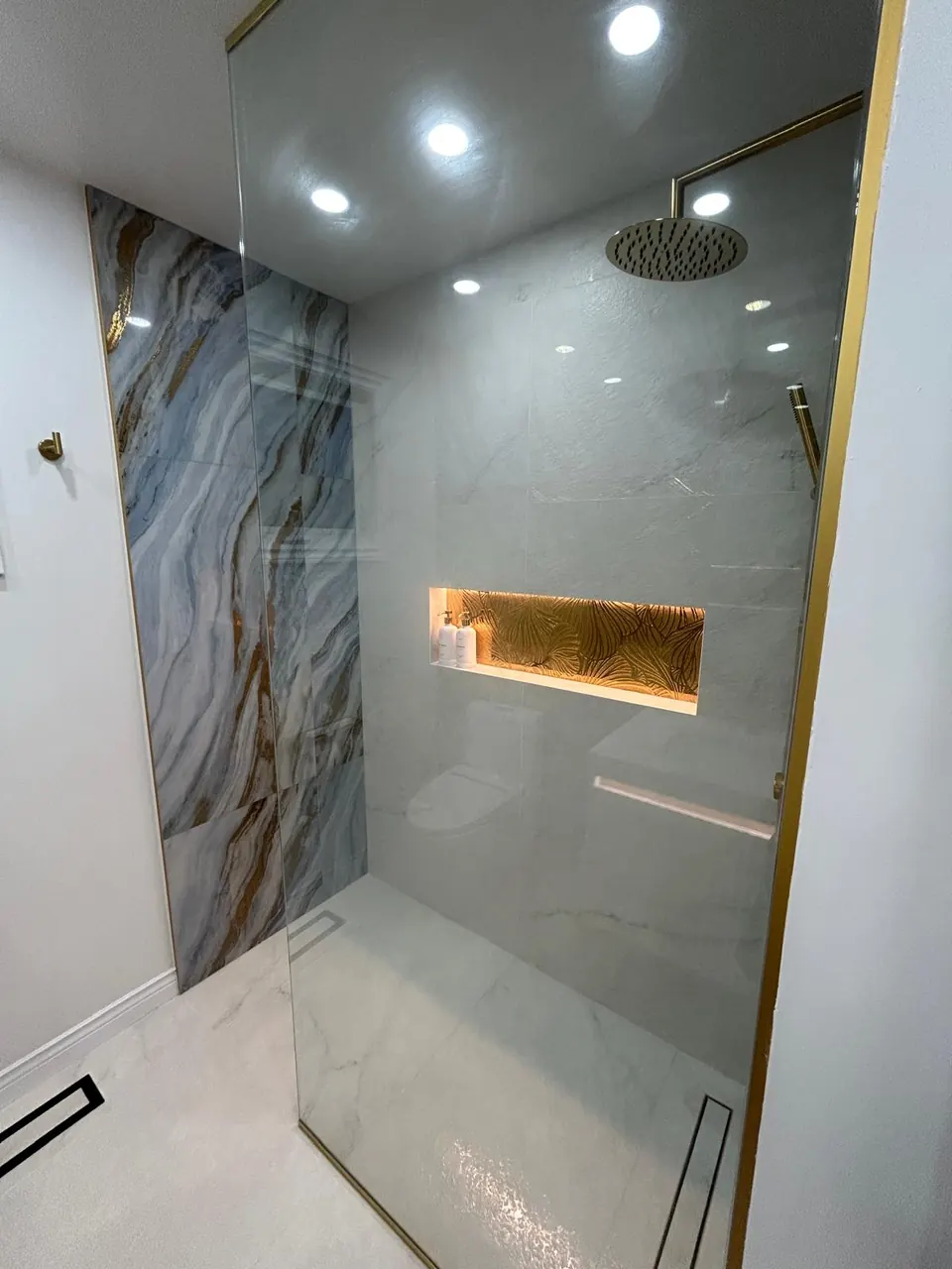 Walk-in shower with lit niche, gold rain head and marble slab wall